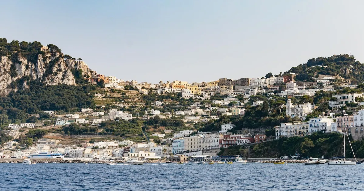 Small tour boat cruising beneath the limestone cliffs of Capri on an island boat trip with grottos around Capri, Italy