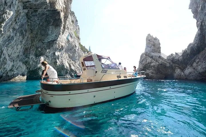 Small wooden gozzo boat anchored off the Faraglioni rocks on a small group Capri island boat ride with swimming in Capri, Italy