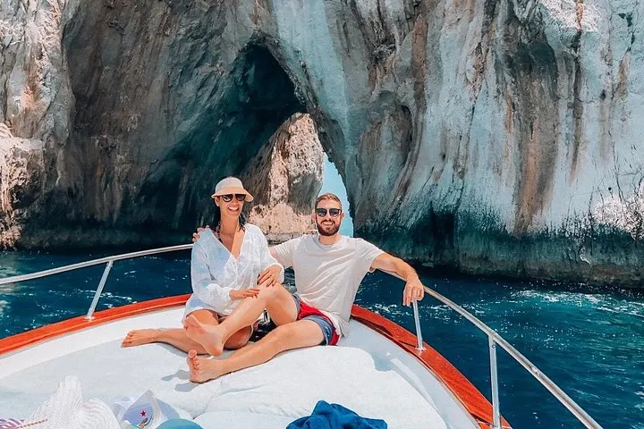 Private gozzo boat cruising beneath the Faraglioni rocks on a private boat tour of Capri, Italy