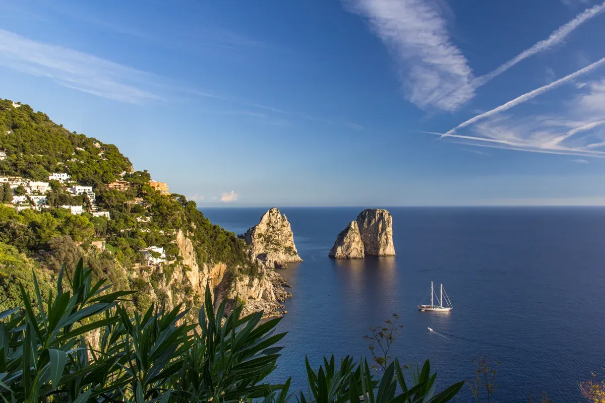 A small private boat passing beneath the Faraglioni stacks on a private boat tour of Capri, Italy